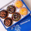Open Borough 22 box of six gluten free vegan fried chocolate doughnuts, chocolate iced rings with rainbow sprinkles, chocolate iced topped with chocolate biscuit pieces, and sugared filled rounds