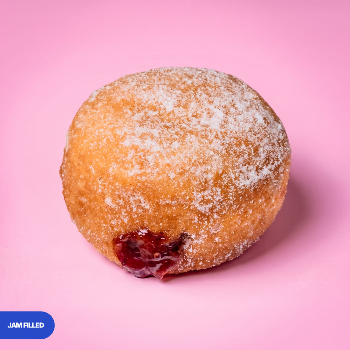 Gluten free vegan fried sugared doughnut filled with raspberry jam, the filling visible at the side
