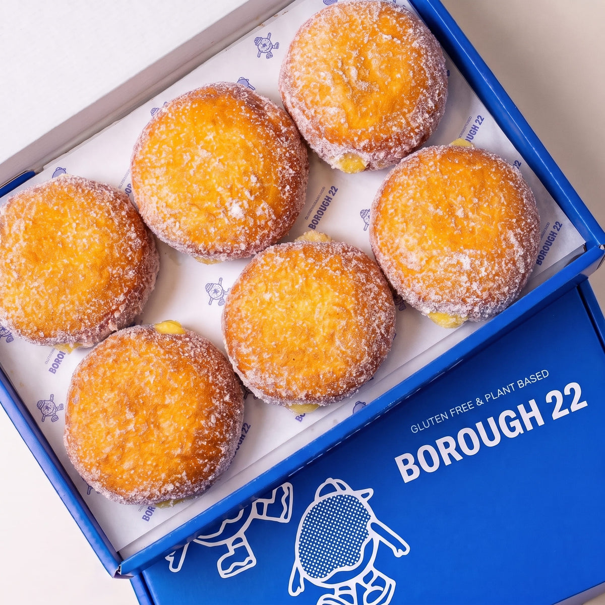 Open Borough 22 box of six gluten free vegan fried sugared doughnuts filled with lemon curd, the filling visible at the side of each one