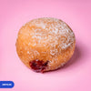 Gluten free vegan fried sugared doughnut filled with raspberry jam, the filling visible at the side